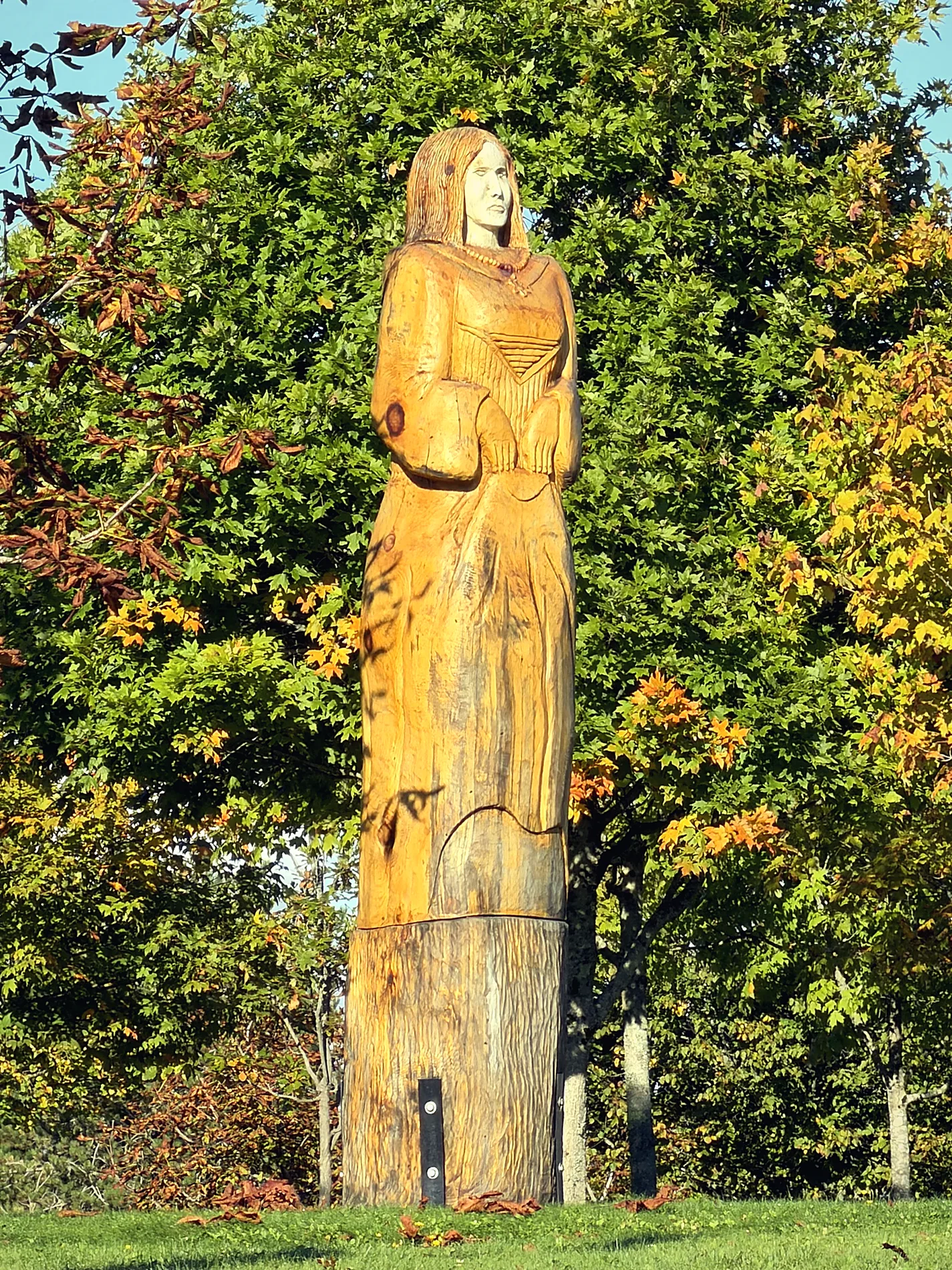 Tall carved wooden statue among autumn trees